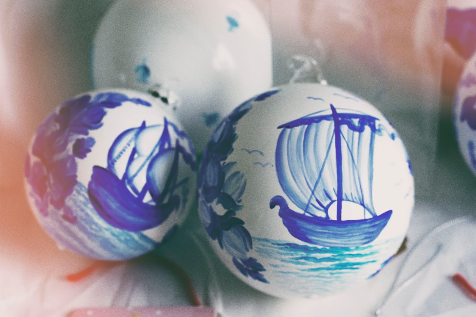 Primer plano de dos adornos blancos pintados a mano con diseños de velero azul y motivos florales, en tonos pastel suaves